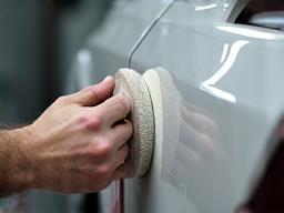 Car body panel being sanded before painting in a workshop.